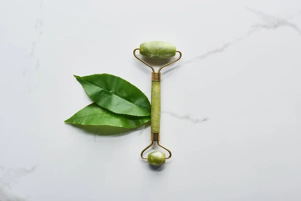 Top view of facial roller and leaves on marble surface — Stock Photo