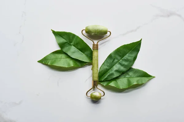 Top view of green facial roller and leaves on marble surface — Stock Photo