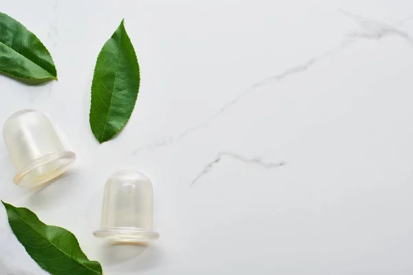 Vista superior de frascos de vacío de masaje y hojas verdes en la superficie de mármol - foto de stock