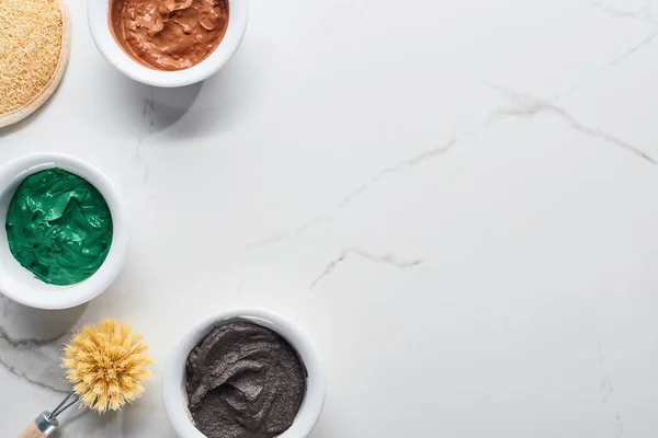 Top view of brown, green and gray face mask near body brush and face sponge on marble surface — Stock Photo