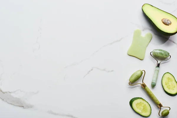 Vista dall'alto di rulli per massaggi e pezzi di cetriolo e avocado sulla superficie di marmo — Foto stock