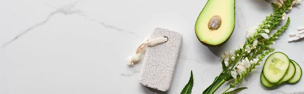 Panoramic shot of pumice stone near avocado, cucumber and fresh branch with flower on marble surface — Stock Photo