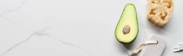 Panoramic shot of half of avocado, loofah and pumice stone on marble surface — Stock Photo