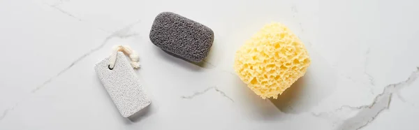Panoramic shot of light and dark gray pumice stone and bath sponge on marble surface — Stock Photo