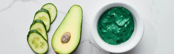 Tiro panorâmico de fatias de pepino, metade de abacate e máscara de rosto verde na superfície de mármore — Fotografia de Stock