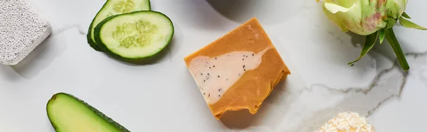 Panoramic shot of natural soap, pumice stone, cucumber slices and rose bud on marble surface — Stock Photo