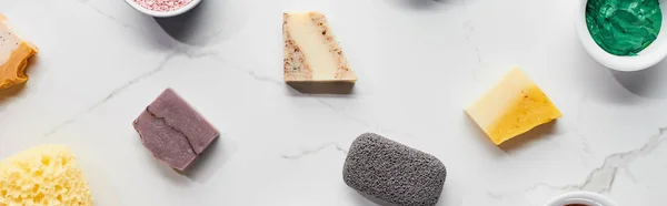 Panoramic shot of diverse soap, pumice stone, bath sponge and clay mask on marble surface — Stock Photo