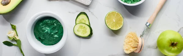 Panoramic shot of natural beauty product and body brush near cucumber slices, lime, avocado and green apple on marble surface — Stock Photo