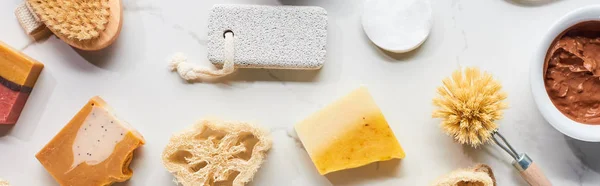 Panoramic shot of loofah, pumice stone, body brushes, cotton pads and homemade soap on marble surface — Stock Photo