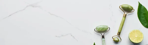 Panoramic shot of green massage rollers near half of lime and green leaf on marble surface — Stock Photo