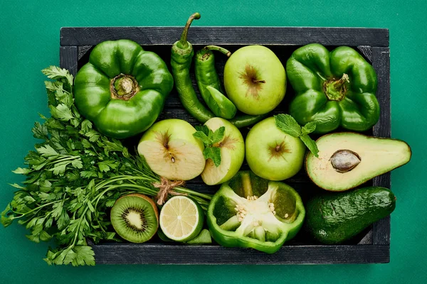 Vista superior de maçãs, abacates, pimentas, kiwi, vegetação, limão e abobrinha em caixa de madeira — Fotografia de Stock