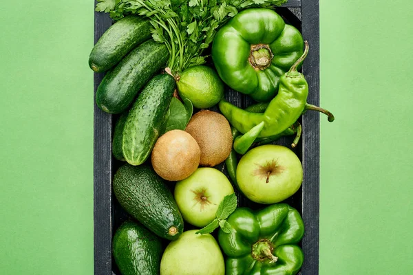 Vista superior de manzanas, aguacates, pepinos, pimientos, kiwi, vegetación y calabacín en caja de madera - foto de stock