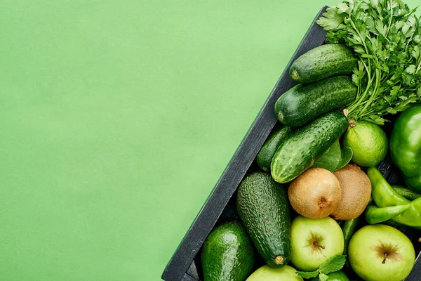 Top view of apples, avocados, cucumbers, peppers, kiwi, greenery in wooden box — Stock Photo