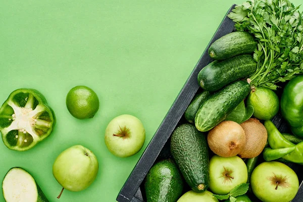 Top view of apples, avocados, cucumbers, peppers, kiwi, greenery in wooden box — Stock Photo