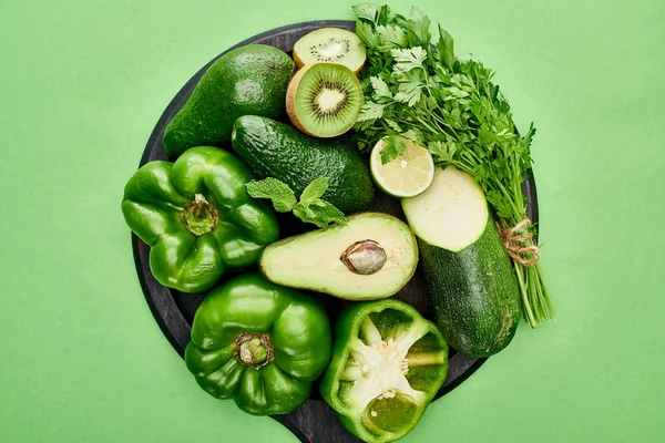 Top view of avocados, peppers, kiwi, lime, zucchini and greenery on pizza skillet — Stock Photo