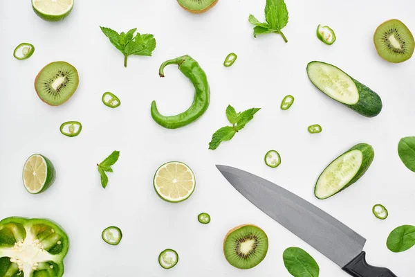 Top view of knife, fresh cucumbers, kiwi, limes, peppers and greenery — Stock Photo