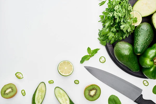Top view of knife, avocados, peppers, kiwi, limes and greenery on pizza skillet — Stock Photo