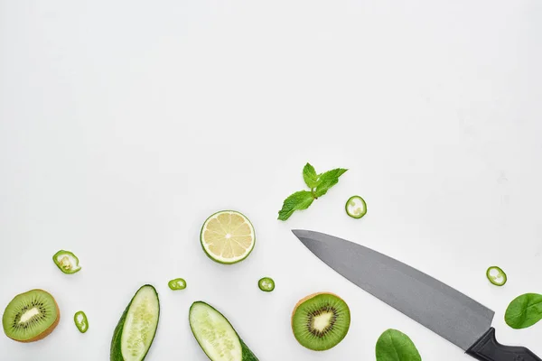 Top view of knife, fresh cucumbers, kiwi, lime, peppers and greenery — Stock Photo