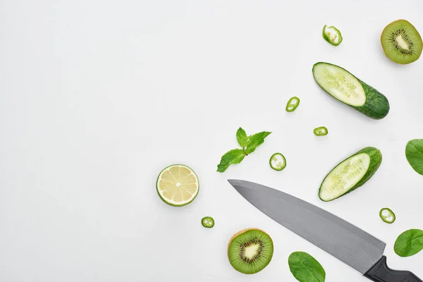 Top view of knife, fresh cucumbers, kiwi, lime, peppers and greenery — Stock Photo