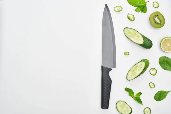 Top view of knife, fresh cucumbers, kiwi, lime, peppers and greenery — Stock Photo