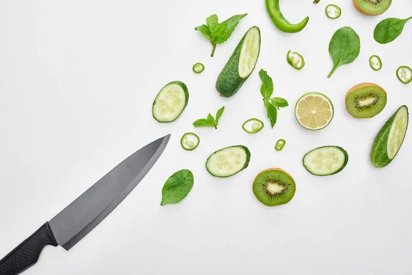 Top view of knife, fresh cucumbers, kiwi, lime, peppers and greenery — Stock Photo