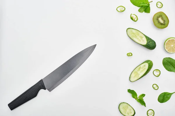 Top view of knife, fresh cucumbers, kiwi, lime, peppers and greenery — Stock Photo