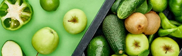 Plano panorámico de manzanas, pimientos, kiwi, vegetación, limas, aguacates en caja de madera - foto de stock