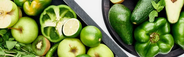 Панорамный снимок авокадо, перца, киви, яблок, лаймов и зелени на сковороде и коробке для пиццы — стоковое фото