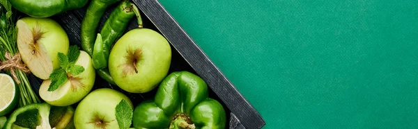Panoramic shot of fresh and green peppers, apples and greenery in wooden box — Stock Photo