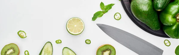 Panoramic shot of knife, fresh cucumbers, kiwi, lime, peppers and greenery on pizza skillet — Stock Photo