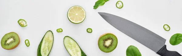 Top view of knife, fresh cucumbers, kiwi, lime, peppers and greenery — Stock Photo