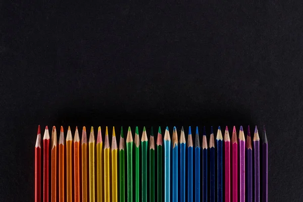 Spectre arc-en-ciel composé d'une rangée droite de crayons de couleur isolés sur du noir — Photo de stock