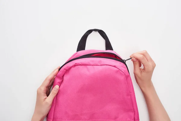 Partial view of schoolgirl zipping bright pink schoolbag isolated on white — Stock Photo
