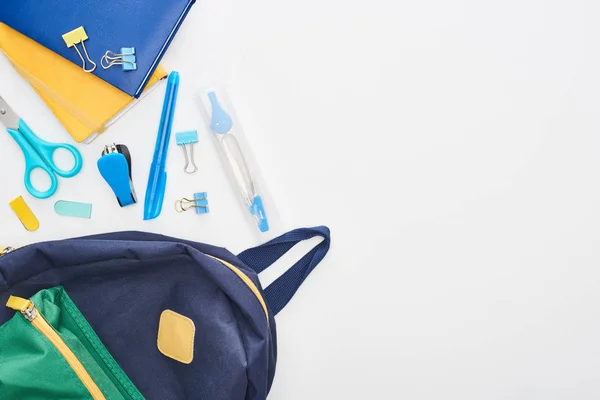 Синя шкільна сумка біля блокнотів, ножиць та різних шкільних приладдя ізольовані на білому — стокове фото