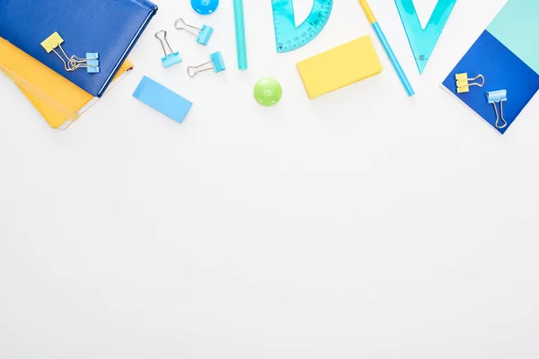 Vue de dessus des fournitures scolaires dispersées bleues et jaunes avec bloc-notes isolés sur blanc — Photo de stock