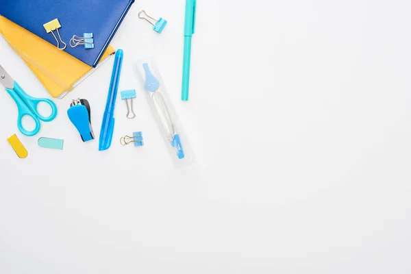 Вид сверху на синие школьные принадлежности рядом с тетрадками, изолированными на белом фоне — стоковое фото