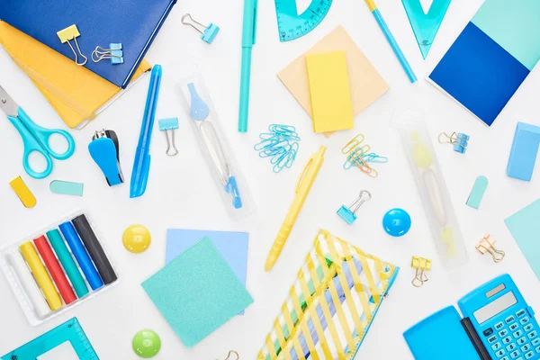 Vista superior de los útiles escolares dispersos azules y amarillos con bloc de notas, estuche de lápiz y calculadora aislados en blanco — Stock Photo