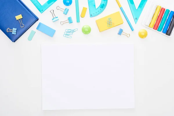 Vue du dessus des fournitures scolaires dispersées bleues et jaunes avec bloc-notes près du papier clair isolé sur blanc — Photo de stock
