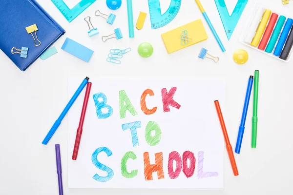 Верхний вид бумаги со школьными надписями рядом с красочными фломастерскими ручками и канцелярскими принадлежностями, изолированными на белом — стоковое фото