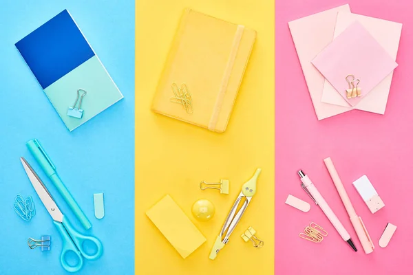 Vista superior de blocos de notas amarelos e azuis perto de folhas de papel rosa com diferentes artigos de papelaria em fundo tricolor — Fotografia de Stock