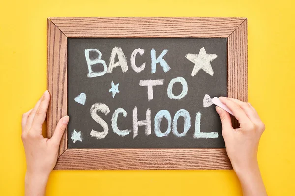 Partial view of schoolgirl writing with chalk back to school text on blackboard — Stock Photo
