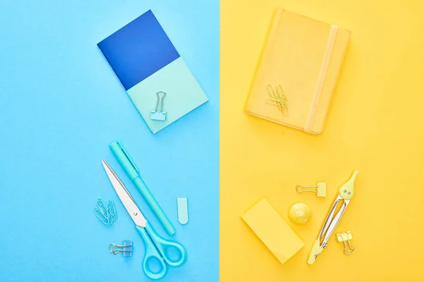Draufsicht auf gelbe und blaue Notizblöcke mit unterschiedlicher Schreibwaren auf zweifarbigem Hintergrund — Stockfoto