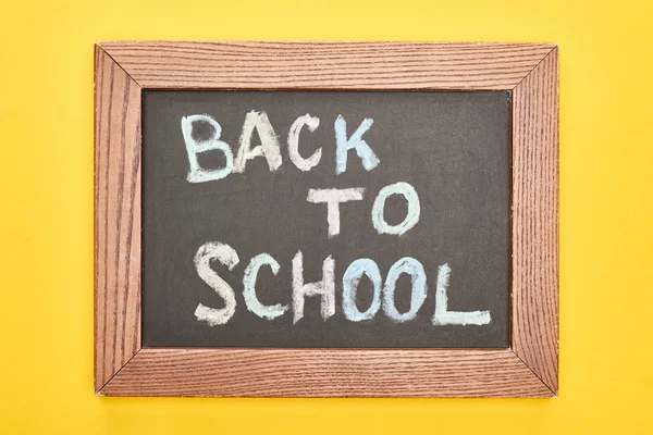 Tableau en bois avec inscription de retour à l'école sur fond jaune — Photo de stock