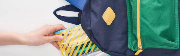Schoolgirl taking yellow pencil case from blue schoolbag isolated on white — Stock Photo