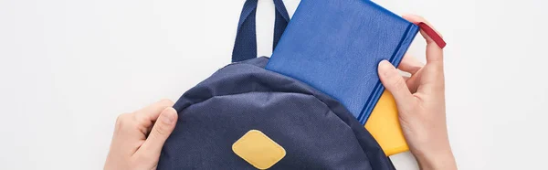 Панорамний знімок школярки, що бере блокнот з синьої шкільної сумки ізольовано на білому — стокове фото