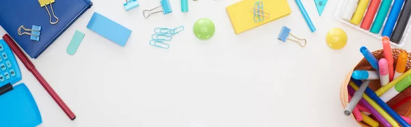 Foto panorámica de materiales escolares dispersos azules y amarillos y taza con coloridos rotuladores aislados en blanco - foto de stock