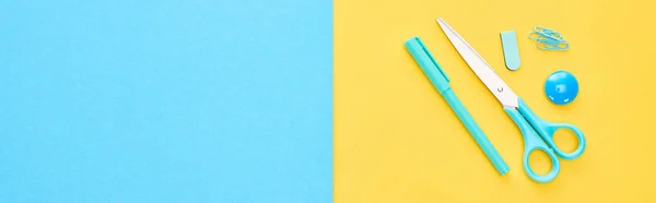 Panoramic shot of blue pen, scissors and paperclips on bicolor background — Stock Photo