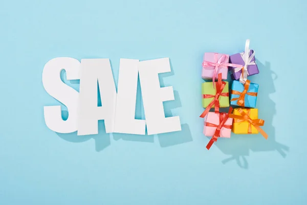 Top view of white sale lettering and festive colorful gift boxes on blue background — Stock Photo