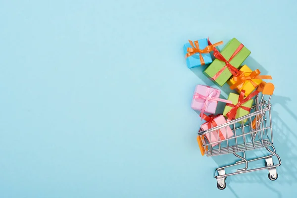 Draufsicht auf bunte festliche Geschenkboxen im Warenkorb auf blauem Hintergrund — Stockfoto