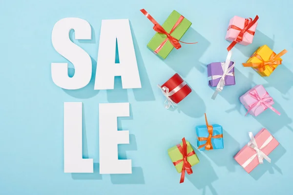 Top view of white sale lettering and festive wrapped presents on blue background — Stock Photo